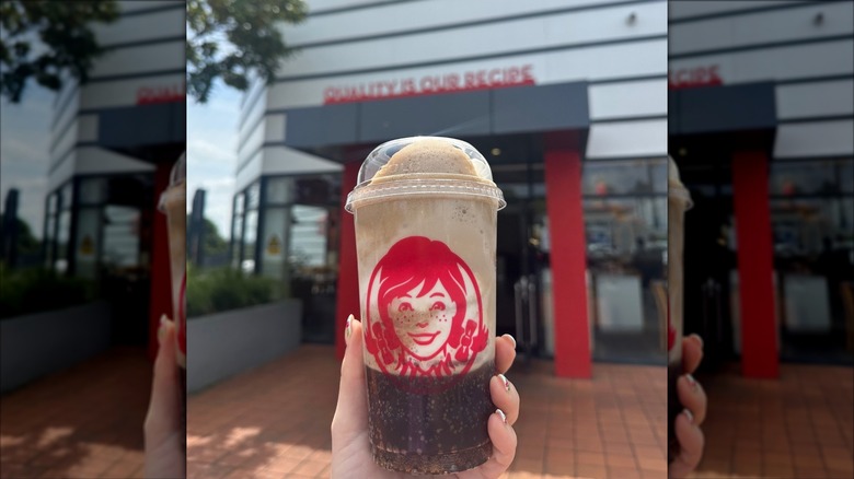 A hand holds a Frosty Float outside a Wendy's restaurant